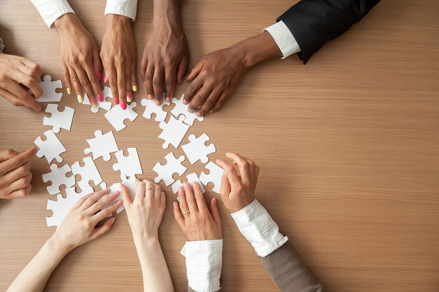 Hands of multi-ethnic business team assembling jigsaw puzzle, top view